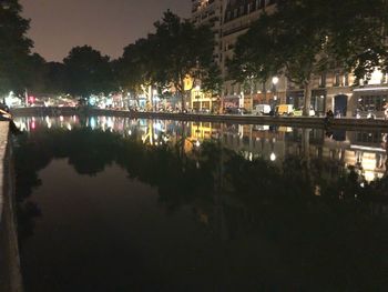 Reflection of trees in lake against sky in city at night