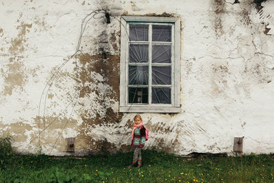 Child on the background of an old cracked wall of a building with a wooden window