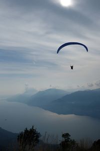 Person paragliding over mountains against sky