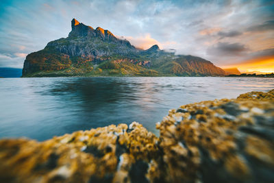 Scenic view of mountain by sea against sky during sunset