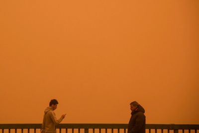 People standing by railing against orange sky