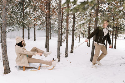 A man and a woman in love have fun and ride a sleigh in the forest among trees in winter in nature