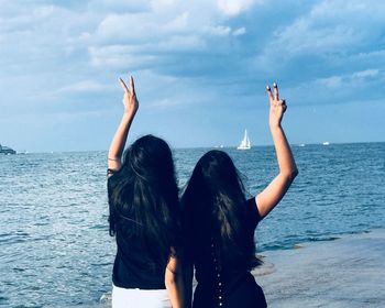 Rear view of female friends gesturing while standing by sea