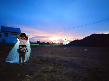 Portrait of girl wearing raincoat while standing on field against cloudy sky during sunset