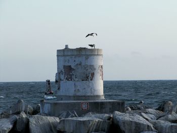 Rocks by storage tank and sea against sky