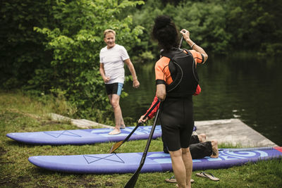 Senior man and woman looking at instructor teaching paddleboarding by sea