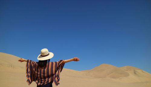 Rear view of woman on desert against clear blue sky