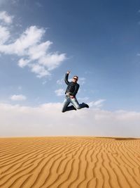 Full length of men walking jump on sand at desert