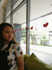 Woman sitting on sofa while looking through window