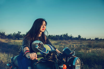 Woman riding motorcycle on field against clear sky
