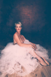 Young woman sitting on floor against gray background