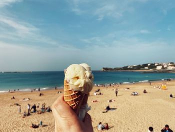 Cropped hand of person holding ice cream against sea and sky