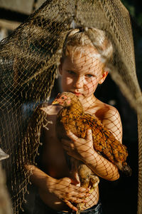 Portrait of shirtless boy holding chicken while standing outdoors