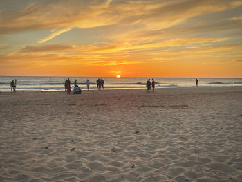 People on beach against sky during sunset