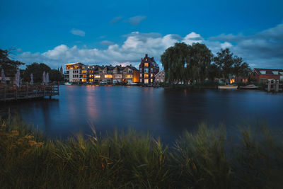 River by illuminated buildings against sky at dusk