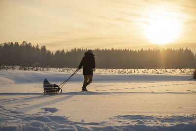 Man on snow covered field against sky during sunset