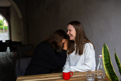 Two young women girlfriends communicate and have fun in a street cafe