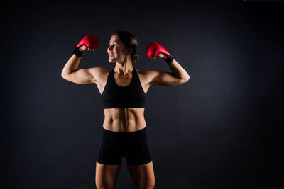 Side view of woman exercising with dumbbells against black background