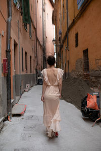 Rear view of woman walking on alley amidst buildings