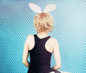 Rear view of woman wearing costume rabbit ears against blue curtain
