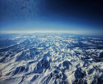 Aerial view of snowcapped mountains against blue sky