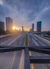 Road by buildings against sky during sunset in city