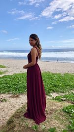 Portrait of young woman standing at beach against sky