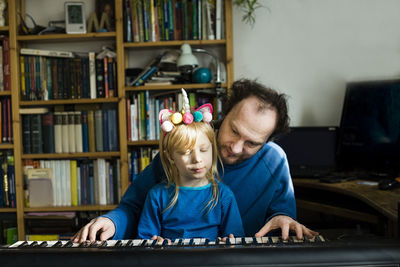 Man teaching synthesizer to daughter while sitting at home