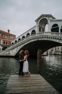 Couple standing on jetty over river against sky