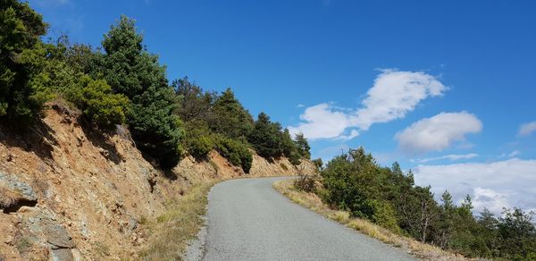 Empty road amidst trees against blue sky