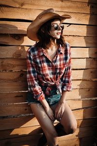 Portrait of young woman sitting on wooden wall