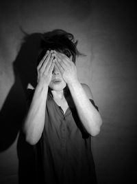 Portrait of woman covering face against wall