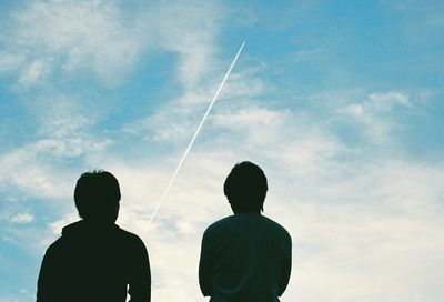Low angle view of men looking at vapor trail in sky