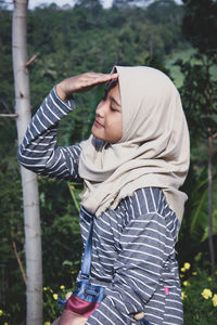 Young woman in hijab saluting against trees