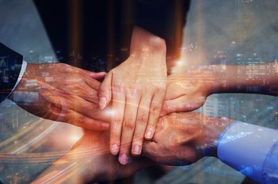 Double exposure image of colleagues stacking hands and cityscape