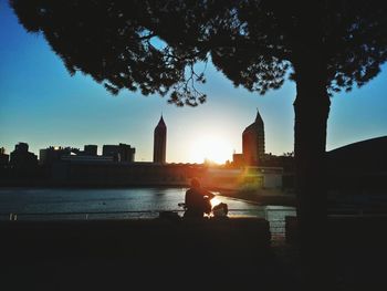 Silhouette of people sitting on river by buildings in city