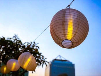 Low angle view of illuminated lanterns hanging by building against sky