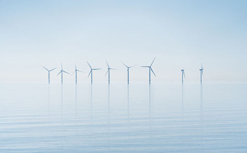 View of wind farm turbines in sun rise haze across still ocean tranquil new energy production