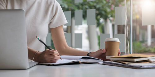 Midsection of woman reading book while sitting on table