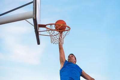 Low angle view of man playing basketball against blue sky