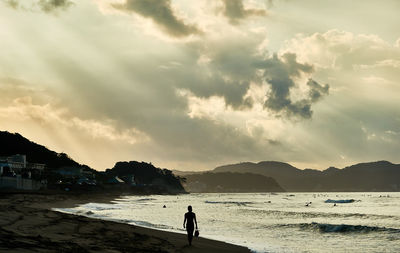 Silhouette man standing on beach against sky during sunrise