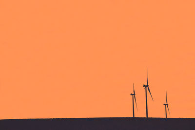 Silhouette of wind turbine against orange sky