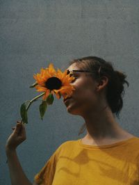 Teenage girl with yellow flower standing against wall