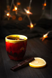 A cup of tea with lemon and chocolate on a dark background with christmas lights