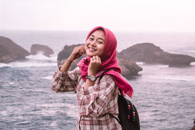 Portrait of smiling young woman standing against sea