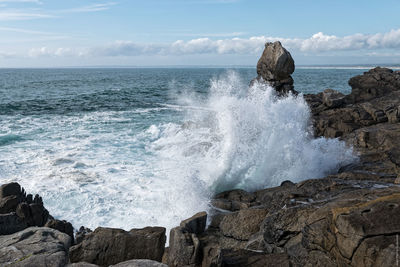 Waves splashing rocks in sea against sky