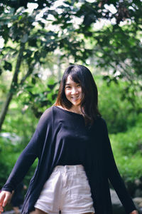 Portrait of young woman standing against trees