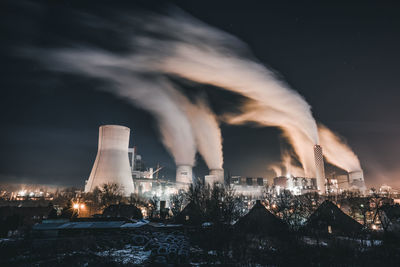 Smoke emitting from illuminated city against sky at night