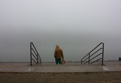 Rear view of man standing on steps during foggy weather