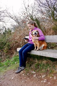 Young woman using mobile with dog while sitting on bench at park